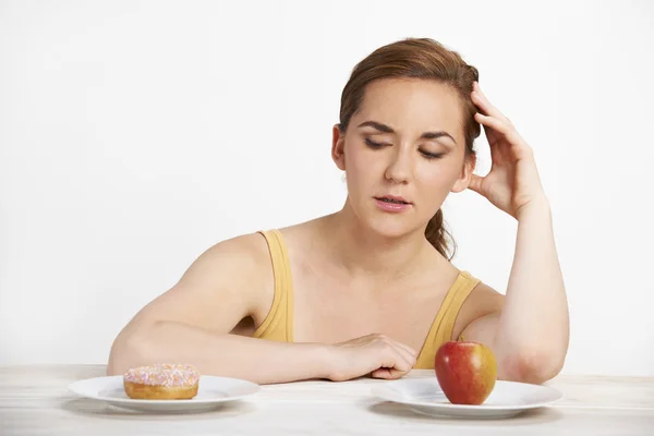 Mulher escolhendo entre maçã e donut para lanche — Fotografia de Stock