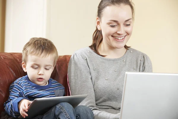 Mutter arbeitet am Laptop, während Sohn digitales Tablet nutzt — Stockfoto