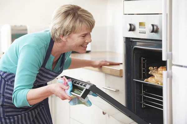 Mulher olhando para assar frango no forno — Fotografia de Stock