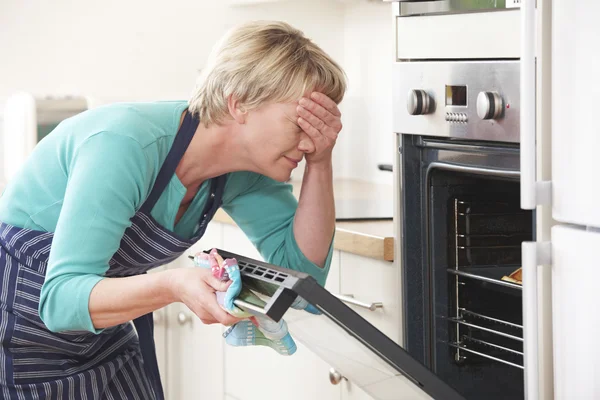 Donna guardando nel forno e coprendo gli occhi sopra pasto disastroso — Foto Stock