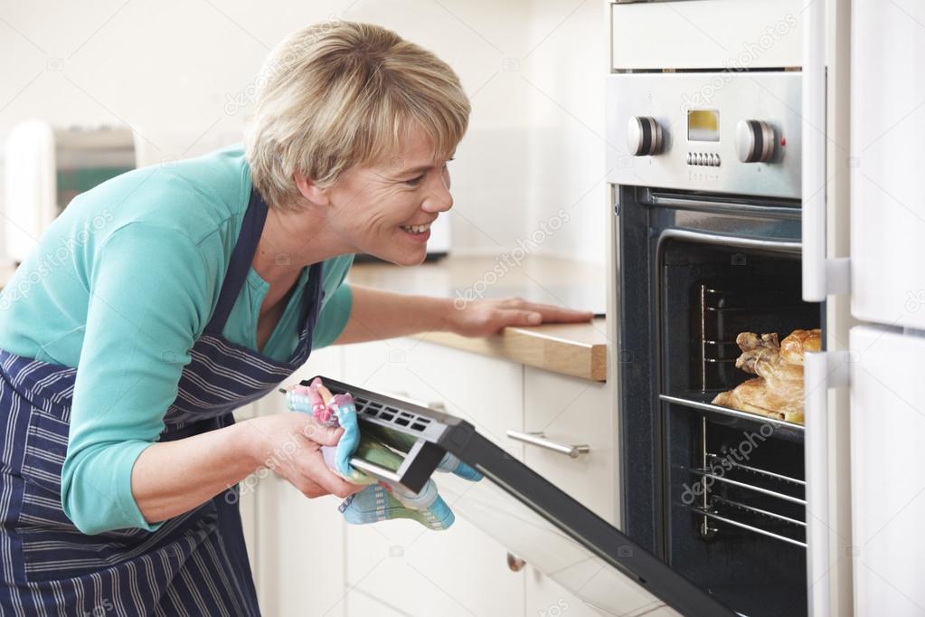 Woman Looking At Chicken Roasting In Oven