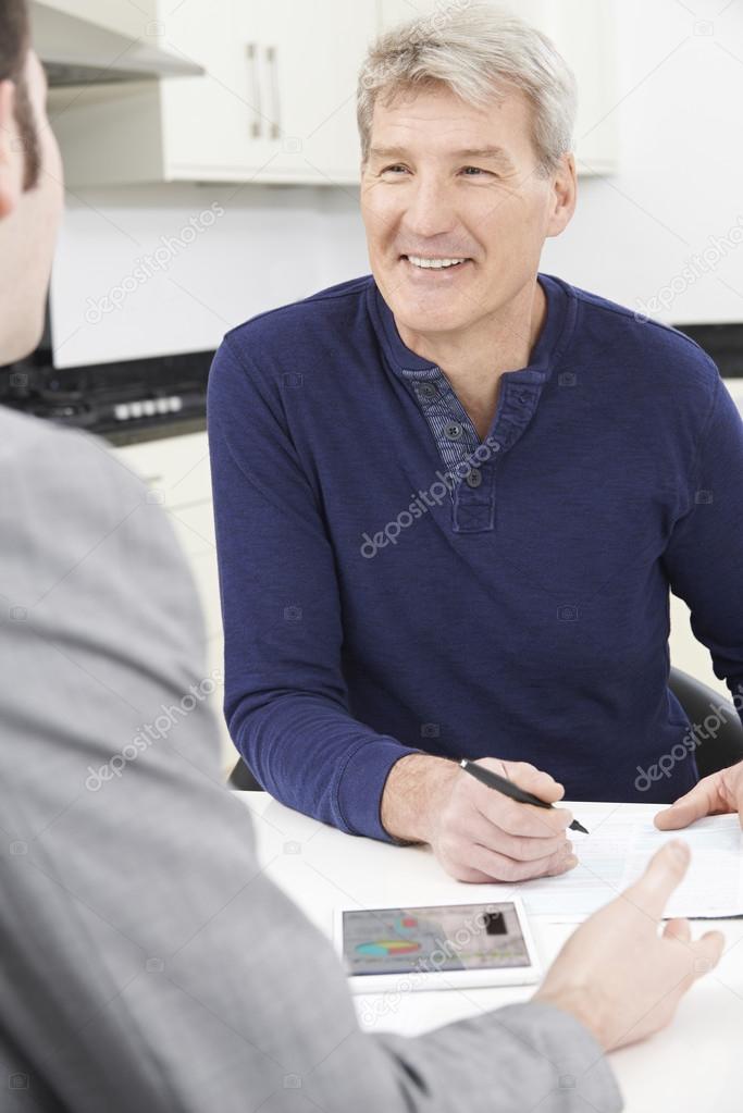 Mature Man With Financial Advisor Signing Document At Home