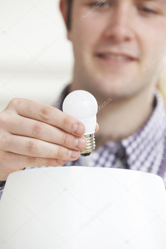 Man Putting Low Energy LED Lightbulb Into Lamp At Home
