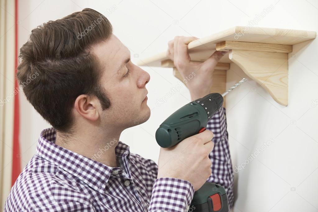 Man Putting Up Wooden Shelf At Home Using Electric Cordless Dril