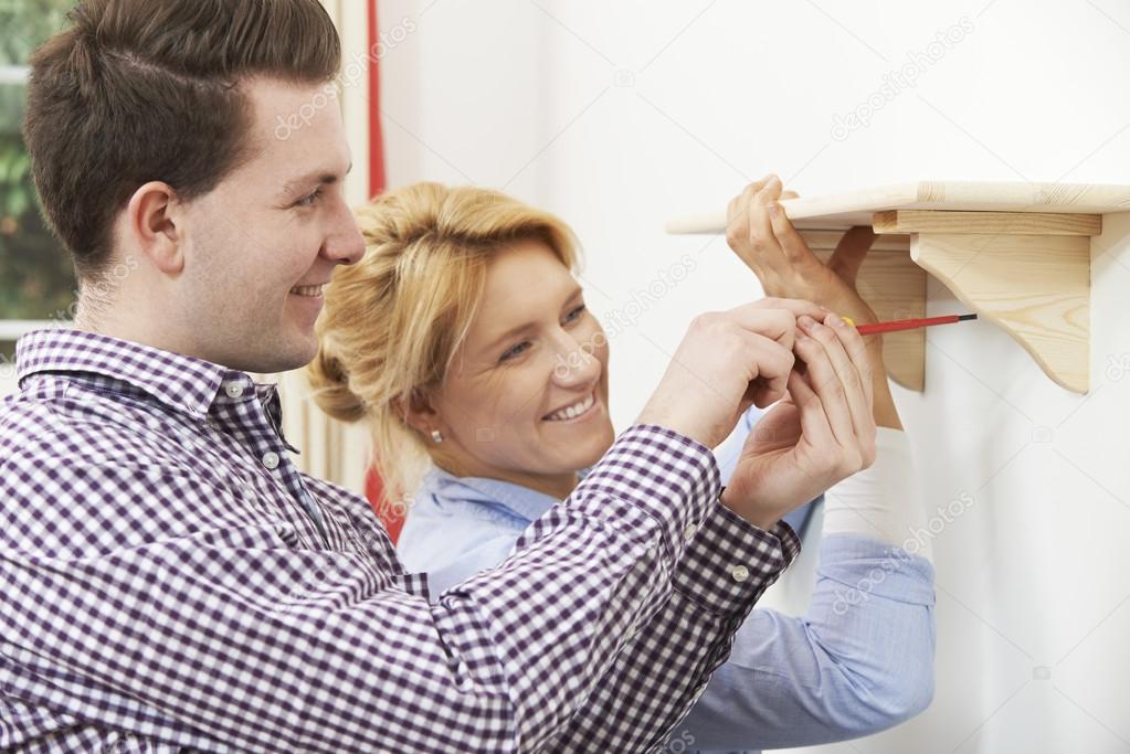 Couple Putting Up Wooden Shelf Together At Home