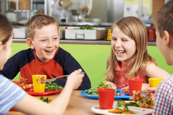 Group Of Pupils Sitting At Table In School Cafeteria Eating Meal