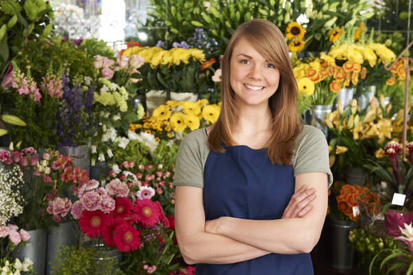Florist Standing In Shop In Front Of Flower Display