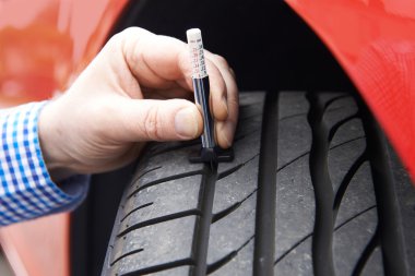 Otomobil lastiğinin lastik izini göstergeyle kontrol eden adama yakın çekim.
