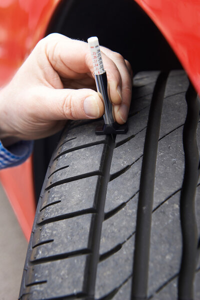 Close-Up Of Man Checking Tread On Car Tyre With Gauge