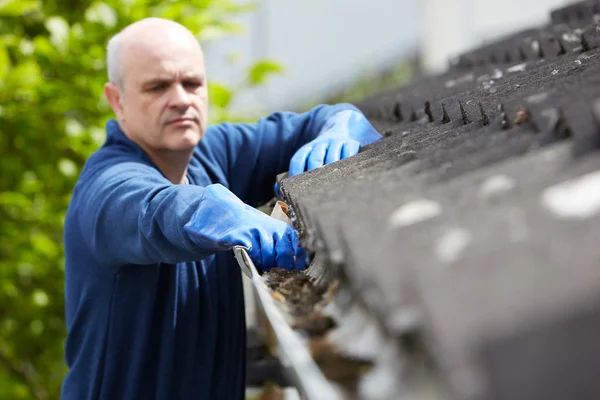 Mann räumt Laub von Dachrinne eines Hauses — Stockfoto