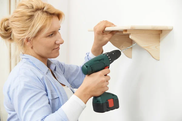 Femme mettant en place une étagère en bois à la maison à l'aide d'une perceuse sans fil — Photo