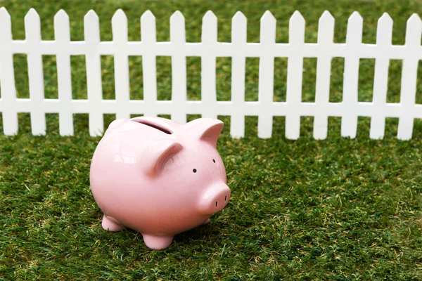 Piggy Bank en la hierba con cerca blanca — Foto de Stock