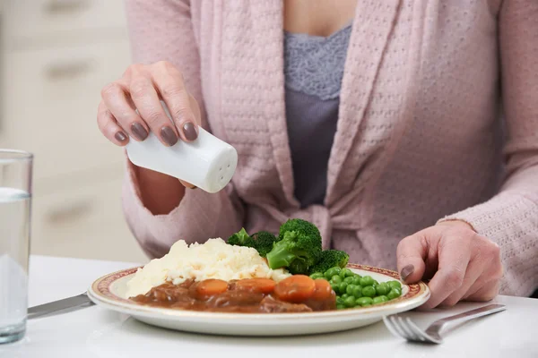 Mujer en casa añadiendo sal a la comida — Foto de Stock