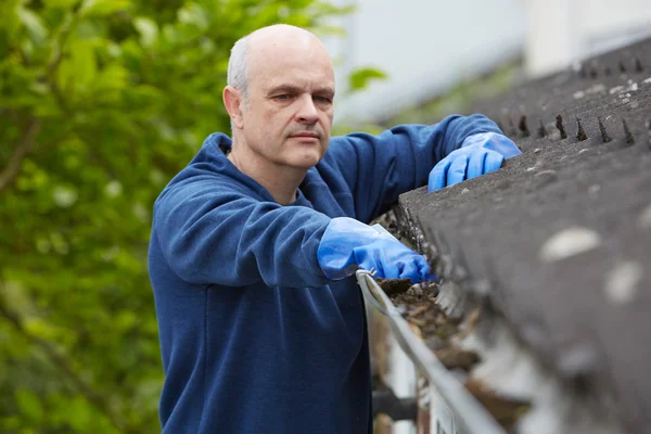 Mann räumt Laub von Dachrinne eines Hauses — Stockfoto