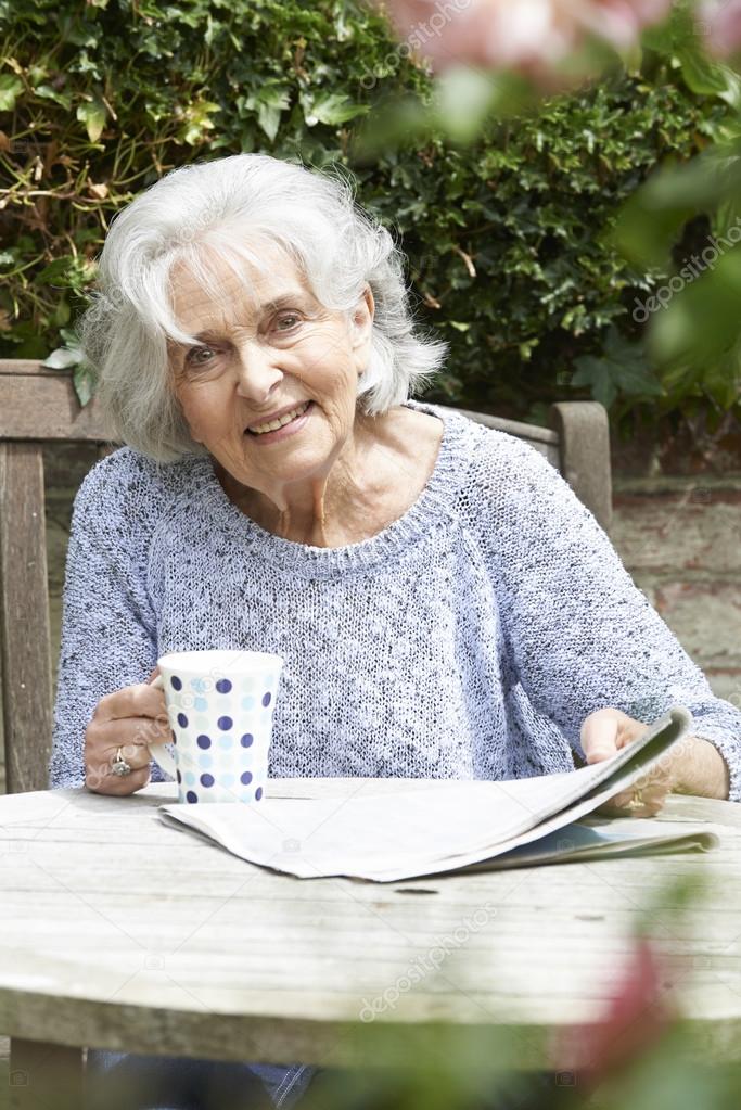 Portrait Of Senior Woman Relaxing In Garden Reading Newspaper