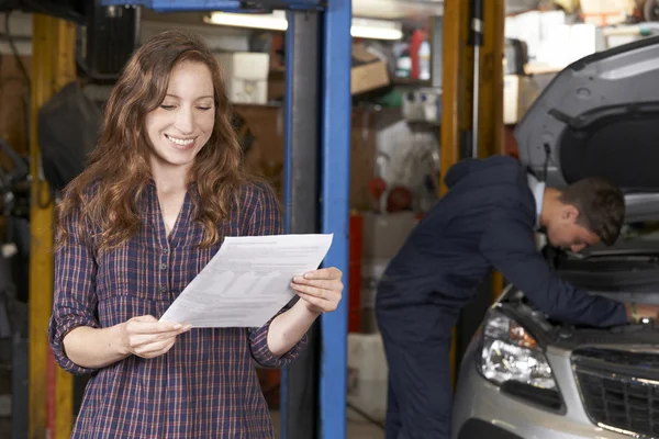 Client féminin dans l'atelier de réparation automobile satisfait de la facture pour la voiture — Photo