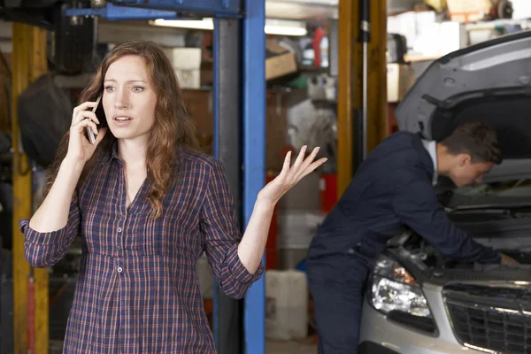 Frustrado cliente femenino en el teléfono móvil en taller de reparación de automóviles — Foto de Stock