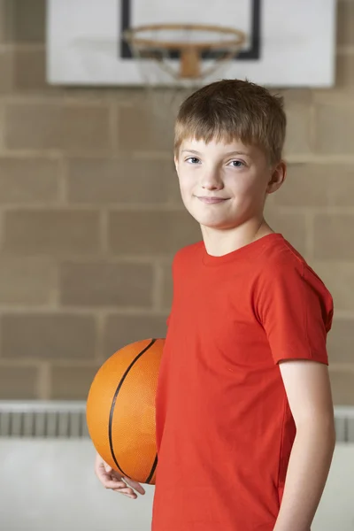 Portret chłopca gospodarstwa koszykówki w sali gimnastycznej szkoły — Zdjęcie stockowe