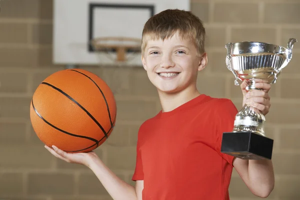 Мальчик проводит баскетбол и трофей в школьной гимназии — стоковое фото