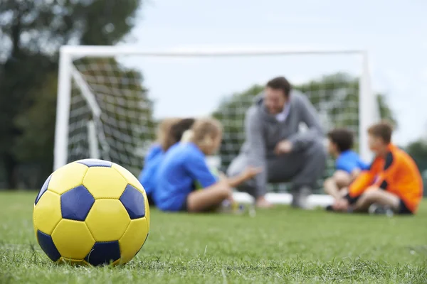 Trainer und Mannschaft diskutieren Fußballtaktik mit Ball im Vordergrund — Stockfoto