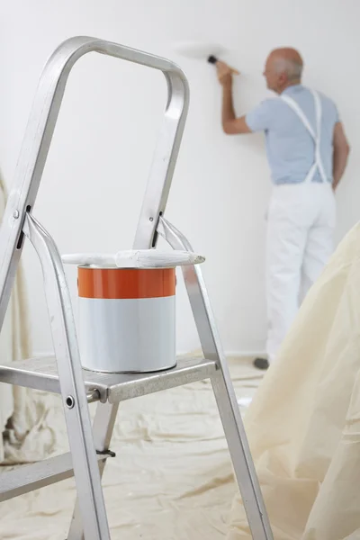 Мужчина украшает комнату банкой краски и кисти на переднем плане — стоковое фото