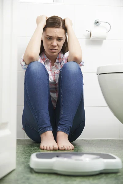 Unhappy Teenage Girl Sitting On Floor Looking At Bathroom Scales — Stock Photo, Image