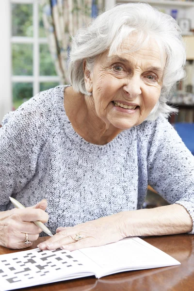 Старшая женщина расслабляется с кроссвордом головоломки дома — стоковое фото