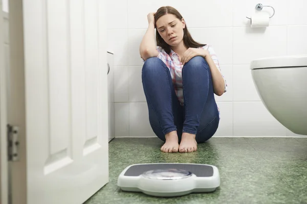 Unhappy Teenage Girl Sitting On Floor Looking At Bathroom Scales — Stock Photo, Image