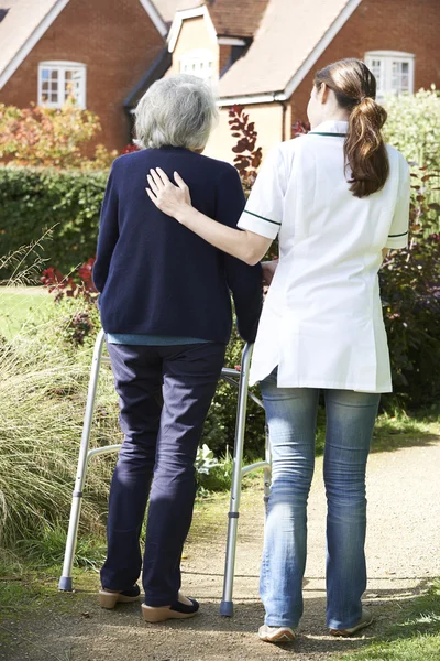Opiekun pomoc starszych kobiety do spaceru w ogrodzie przy chodzenie ramki — Zdjęcie stockowe