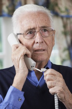 Worried Senior Man Answering Telephone At Home clipart