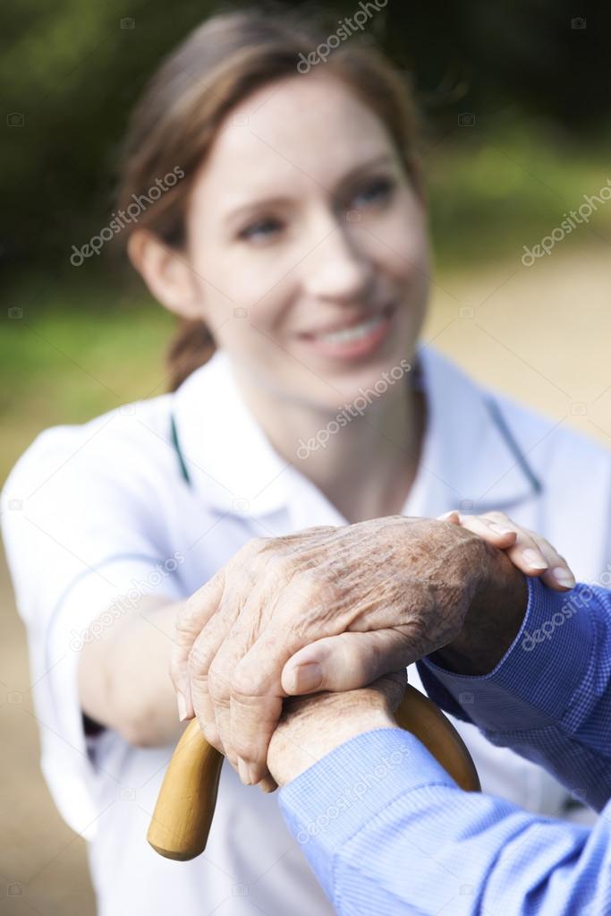 Senior Man's Hands Resting On Walking Stick With Care Worker In