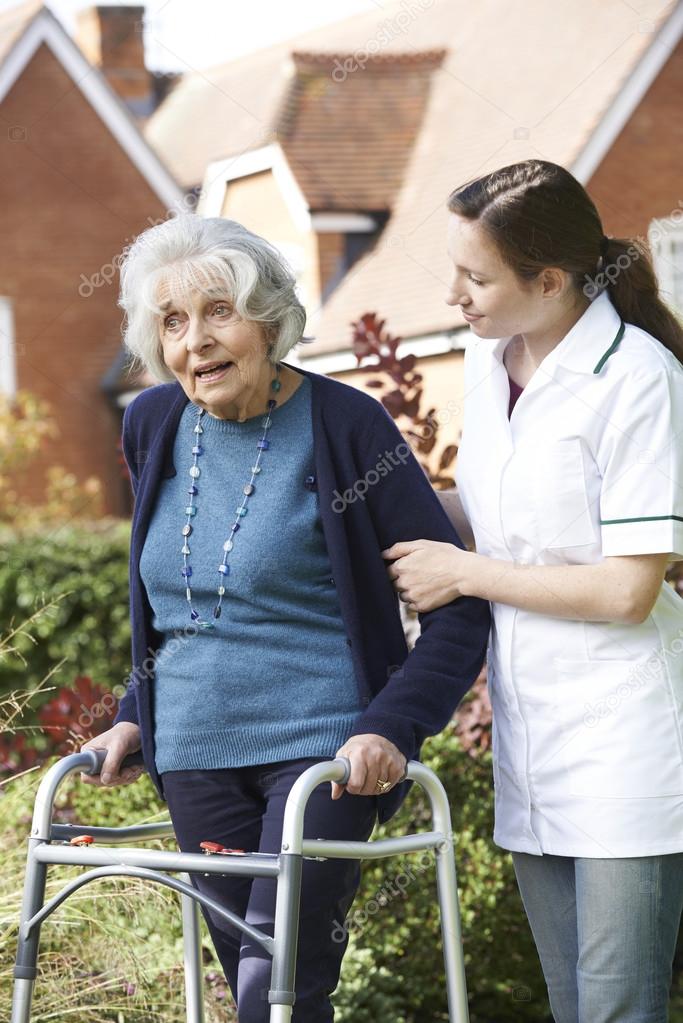 Carer Helping Senior Woman To Walk In Garden Using Walking Frame
