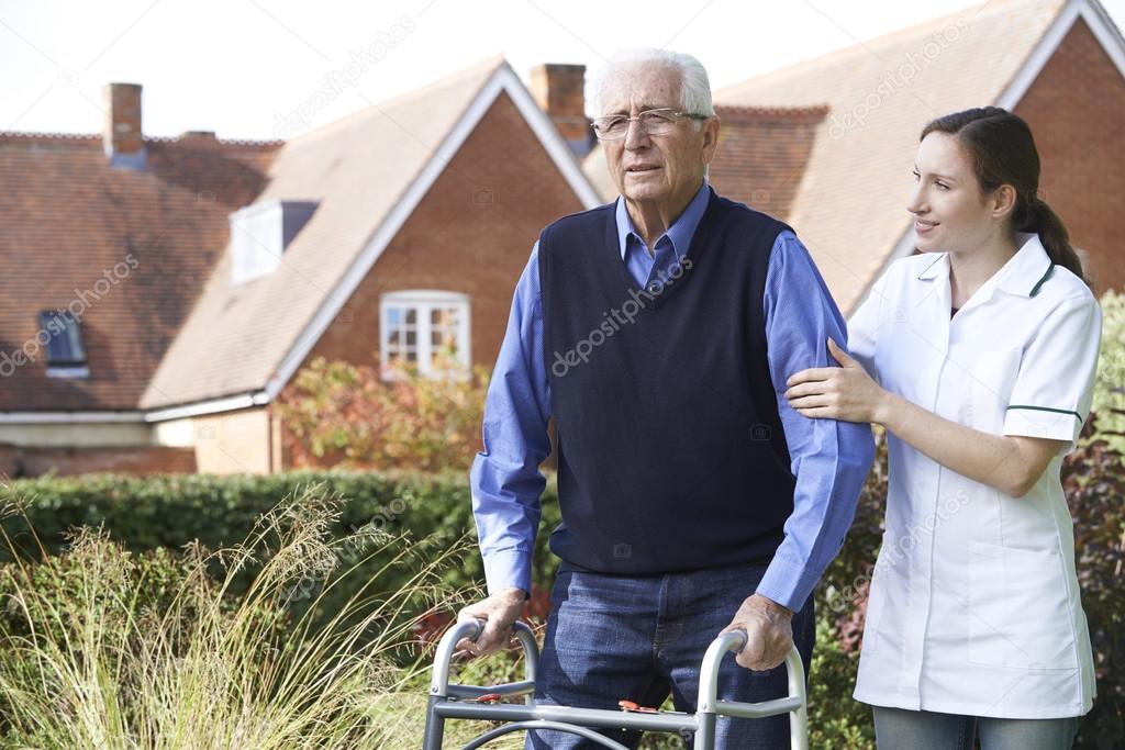 Carer Helping Senior Man To Walk In Garden Using Walking Frame