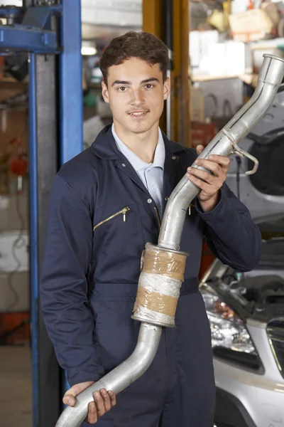 Učeň mechanik drží výfukového potrubí v Auto opravna — Stock fotografie