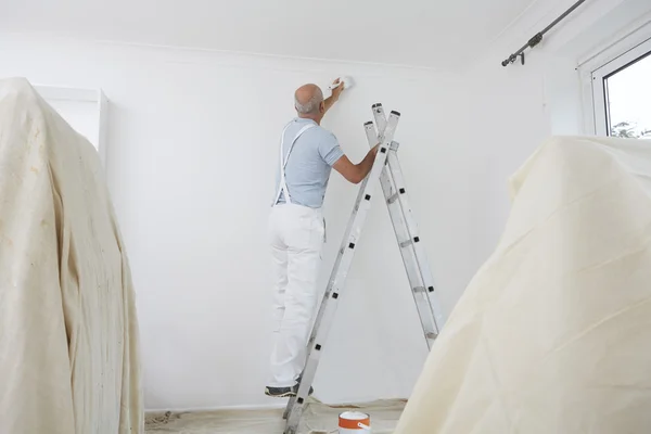 Mann auf Leiter dekoriert Wohnzimmer mit Pinsel — Stockfoto