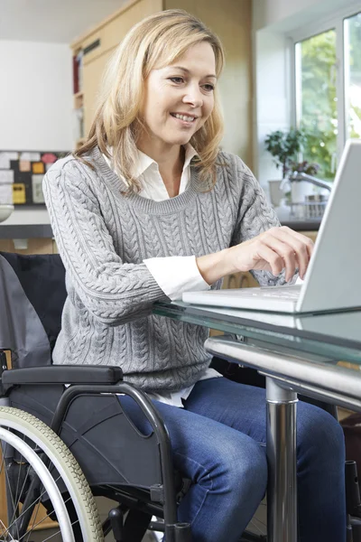 Жінка з обмеженими можливостями у інвалідному кріслі, використовуючи ноутбук вдома — стокове фото