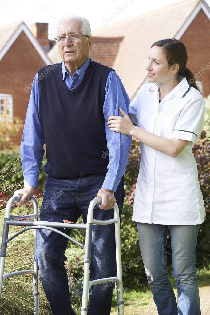 Carer Helping Senior Man To Walk In Garden Using Walking Frame