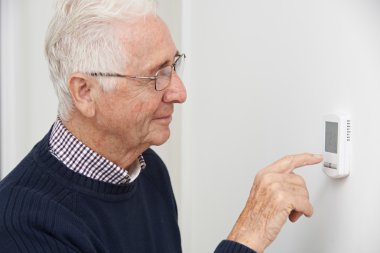 Smiling Senior Man Adjusting Central Heating Thermostat clipart