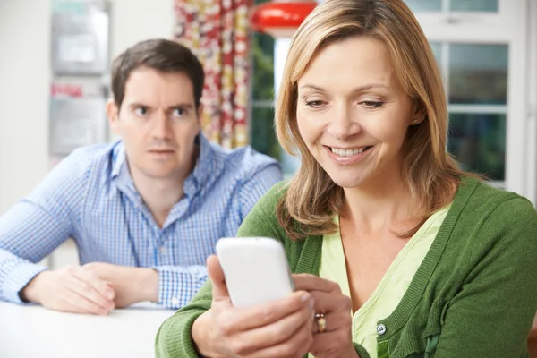 Hombre infeliz sentado en la mesa como compañero de texto en el teléfono móvil — Foto de Stock