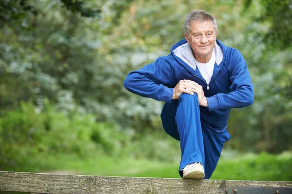 Uomo anziano che si estende sulla campagna correre — Foto Stock