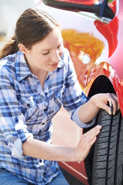 Woman Checking Tread On Car Tyre With Gauge