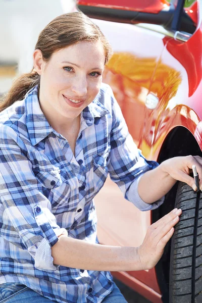 Mujer que comprueba la huella en el neumático del coche con el indicador — Foto de Stock