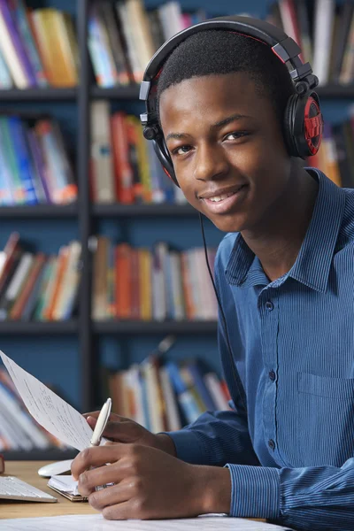 Estudiante adolescente usando auriculares mientras trabaja en la biblioteca — Foto de Stock