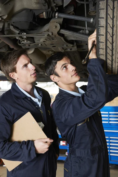 Mecánico y aprendiz trabajando debajo del coche — Foto de Stock