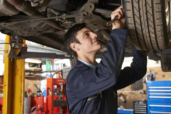 Aprendiz mecánico trabajando debajo del coche — Foto de Stock