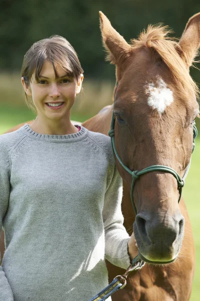 Jovem mulher segurando cavalo no campo — Fotografia de Stock