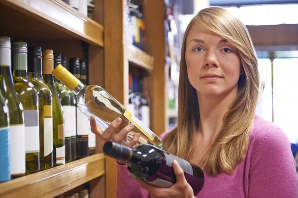 Женщина выбирает между красным и белым вином в супермаркете — стоковое фото