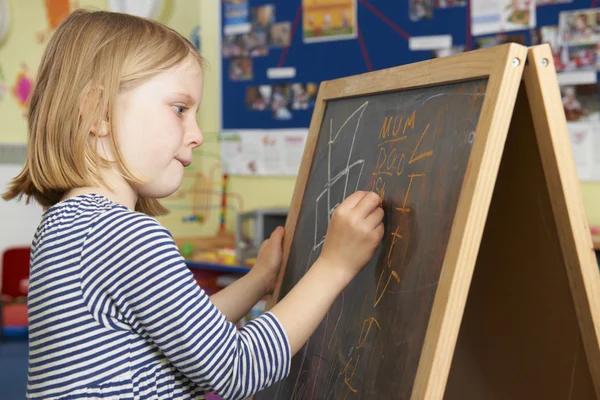 Ung flicka skriver på svarta tavlan i skolan klassrum — Stockfoto