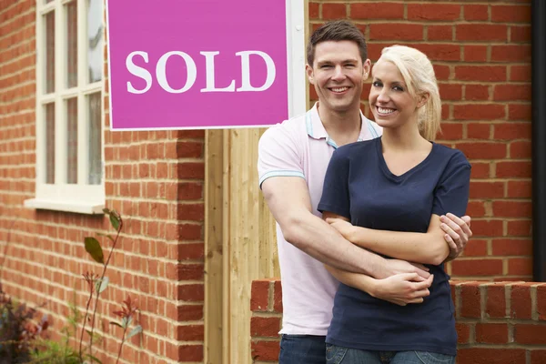 Glückliches junges Paar steht neben verkauftem Schild vor neuem Zuhause — Stockfoto