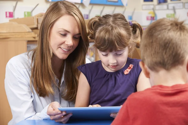 Profesor ayudando a los alumnos de primaria a usar la tableta digital — Foto de Stock